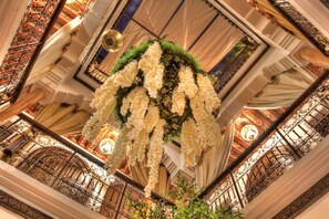 A grand interior with ornate iron railings, a floral arrangement, and a chandelier.