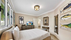 A bedroom with a large bed, a television, a desk, and artwork on the walls. - Aruba Oasis! 3BR Home w Pool & BBQ near Palm Beach (Noord)