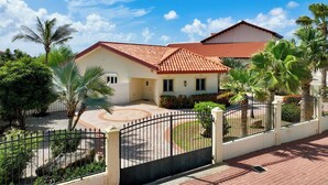 A two-story house with a red-tiled roof, a paved driveway, and a fenced garden area. - Aruba Oasis! 3BR Home w Pool & BBQ near Palm Beach (Noord)