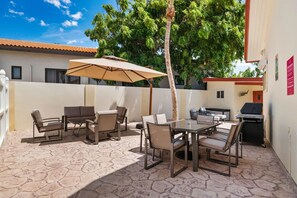 Eine Terrasse im Freien mit Tisch und Stühlen, einem Grill und einer Palme.