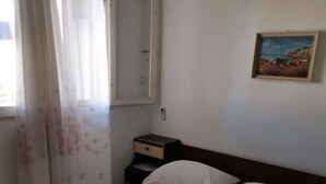Una habitación de hotel con cama, mesita de noche, un cuadro en la pared y un equipo de aire acondicionado.