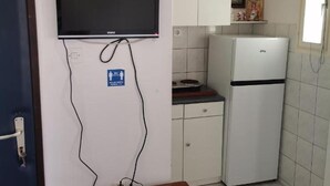 Una cocina pequeña con un refrigerador blanco, un microondas y un lavamanos. Hay un televisor montado en la pared y una pequeña mesa con una regleta de enchufes y controles remotos.