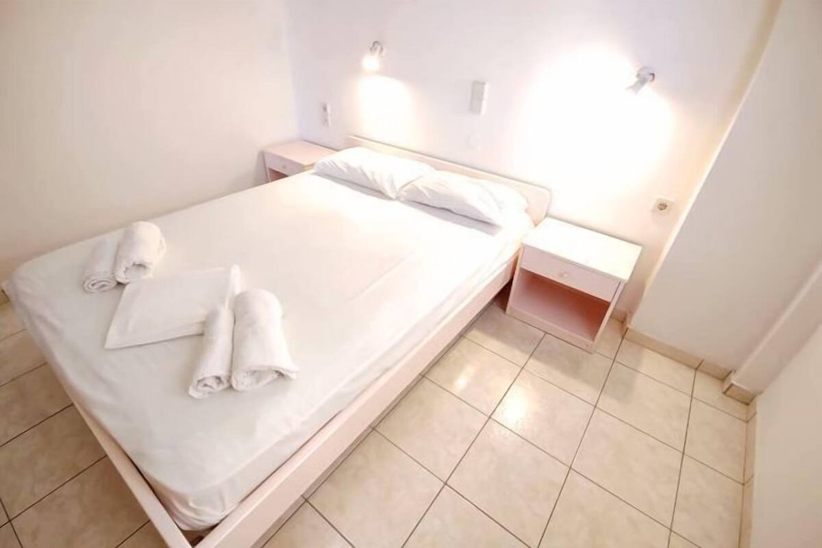 A neatly made bed with white linens and towels, a bedside table, and a nightstand.