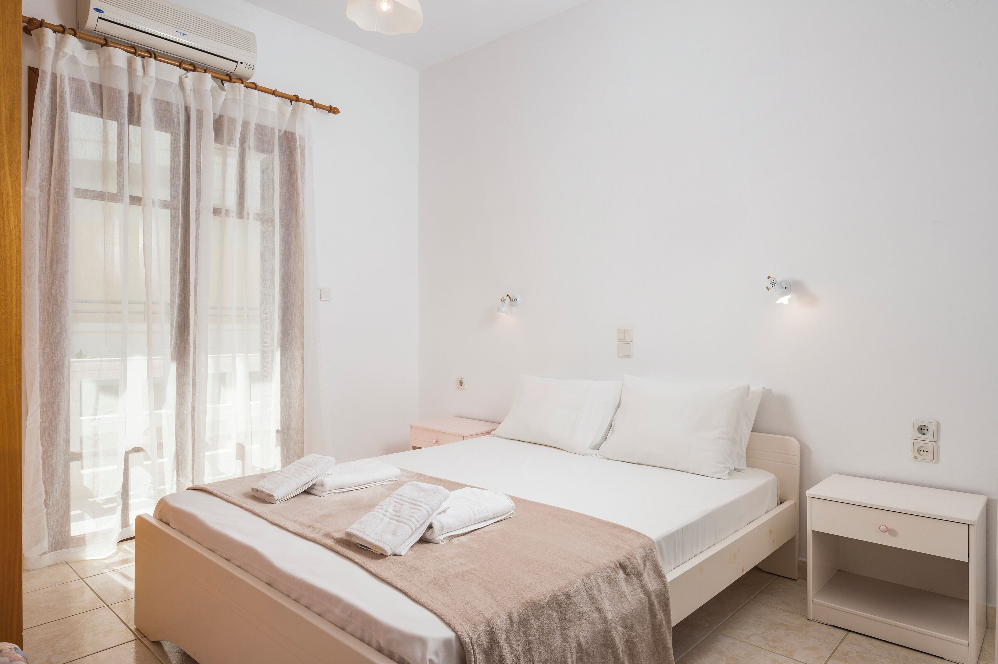 Une chambre d’hôtel au design minimaliste, comprenant un lit, des tables de chevet et une fenêtre ornée de rideaux légers.