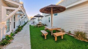 Une rangée de bâtiments blancs, avec une pelouse verte, des tables de pique-nique en bois et des parasols.