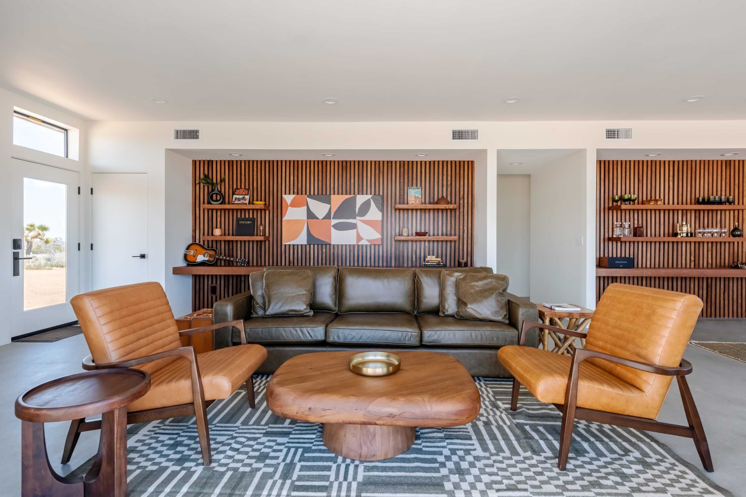 Una sala de estar moderna con un sofá de cuero, dos sillones de cuero, una mesa de centro de madera y estanterías empotradas con objetos decorativos.