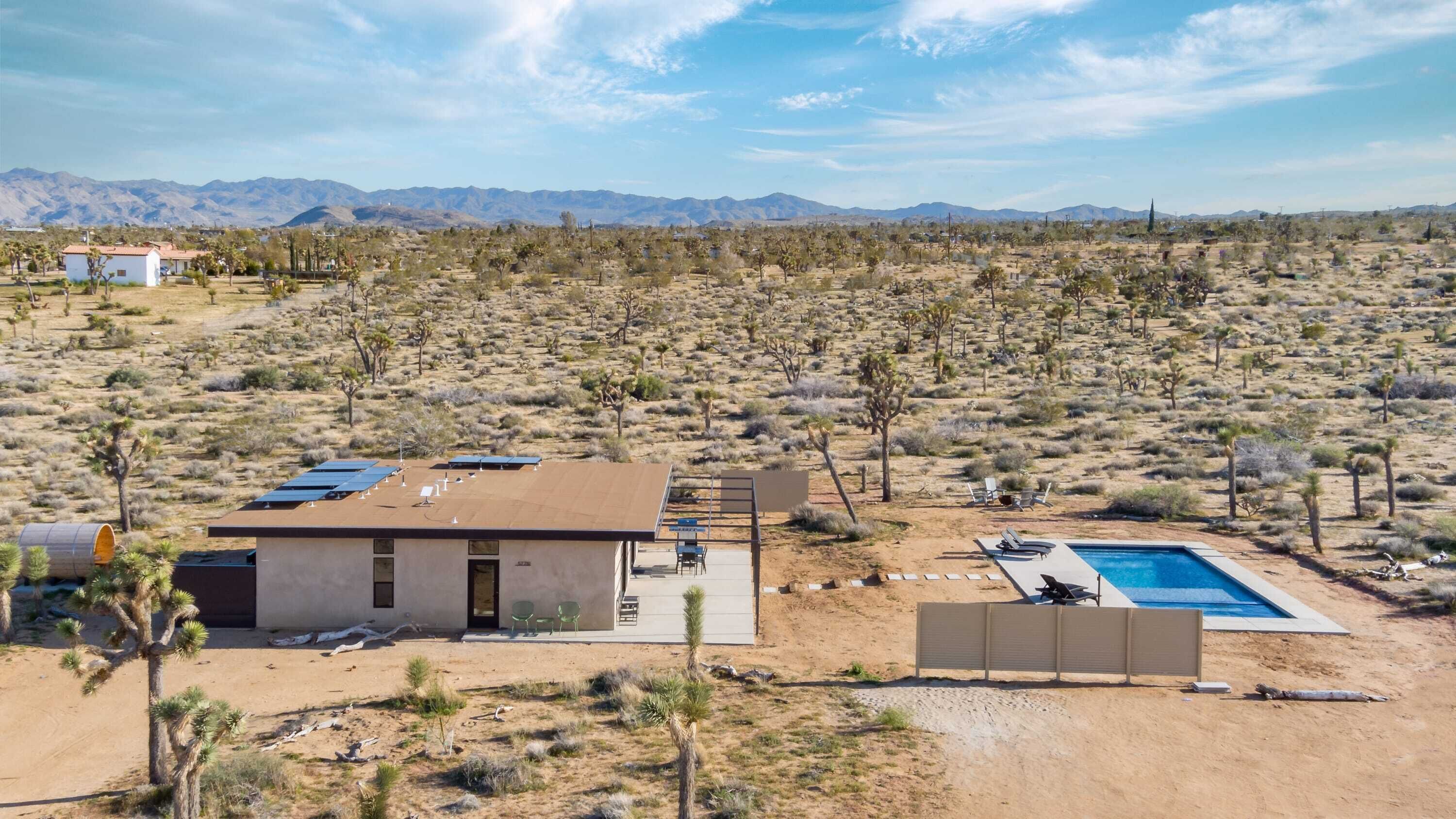 A desert landscape with a single-story building featuring a pool and solar panels.