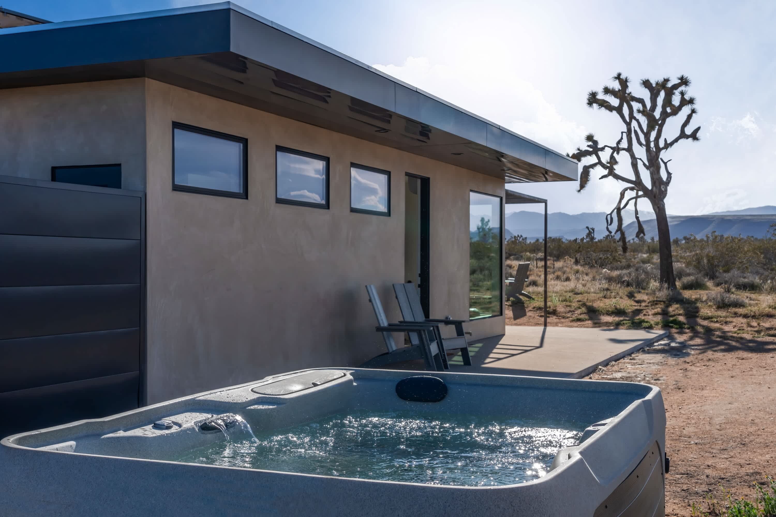 Un edificio moderno con idromassaggio, area salotto esterna e un paesaggio desertico con un Joshua tree.