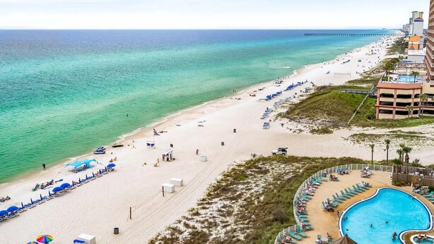 A beach resort with a swimming pool, beach umbrellas, and a pier in the background. - Emerald Beach Resort 1133 - Beachfront on the 'Main Strip'! (Panama City Beach)
