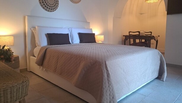 A bedroom with a large bed, a small table, and a chair. - Viale del Sole - le Dimore - Small Double Room (Locorotondo)