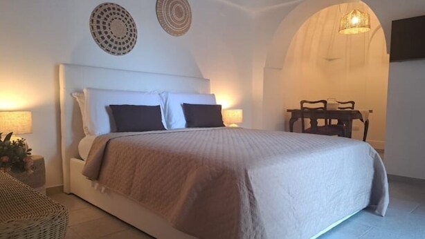 Une chambre à coucher avec un grand lit, deux tables de chevet avec des lampes, une petite table avec une plante et une chaise.
