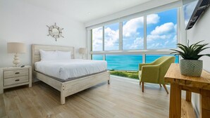 Ein Schlafzimmer mit großem Fenster und Meerblick, ein Bett, ein Nachttisch, ein Sessel und ein kleiner Tisch mit Pflanze.