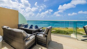 Ein Balkon mit Korbmöbeln, einem Glastisch und Blick aufs Meer.