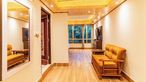 A modern living room with wooden flooring, a sofa, a TV, and a window with a view of trees. - The Golden Retreat Hotel in Pelling (Gyalshing)