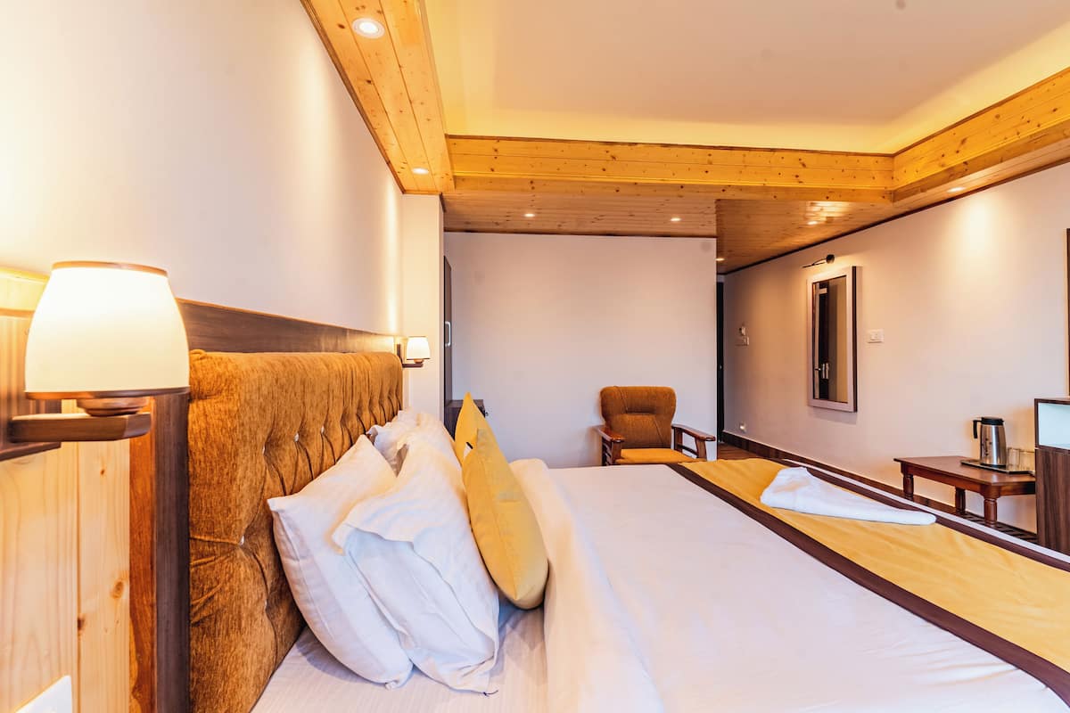 A hotel room with a large bed, a wooden headboard, a bedside lamp, a chair, a desk, and a mirror.