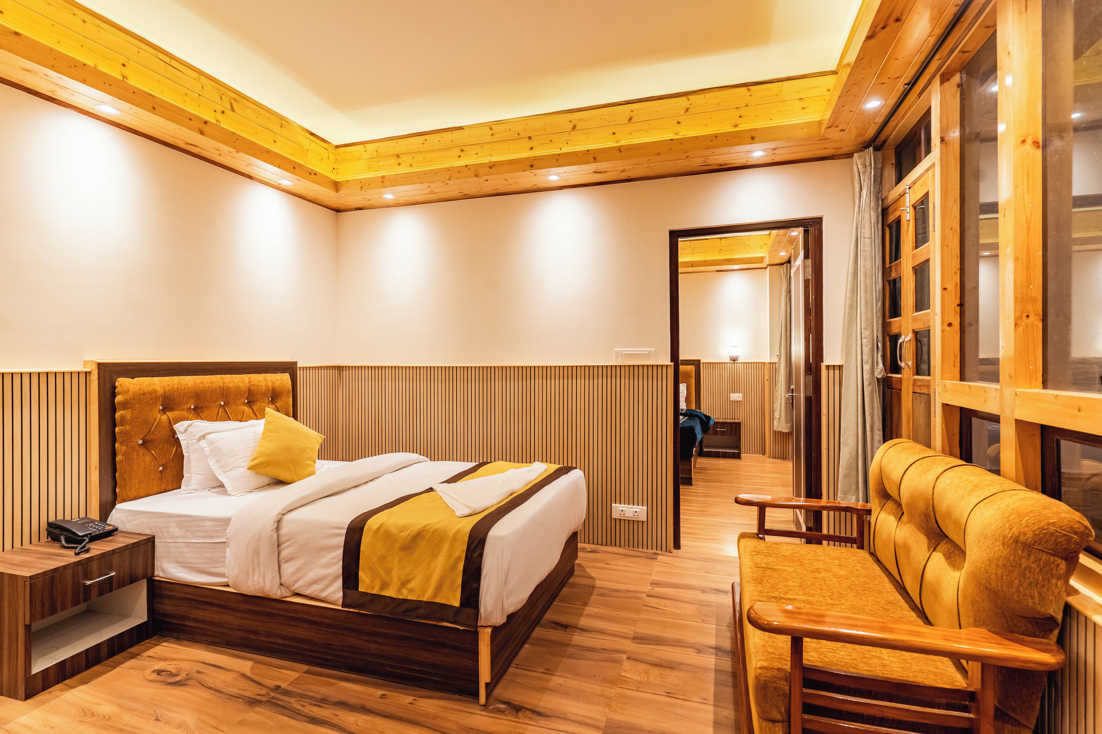 A hotel room with a wooden bed, a wooden nightstand, a wooden chair, and a wooden floor.