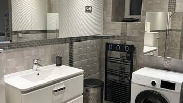 Une salle de bain moderne avec un grand miroir, un lavabo, un lave-linge et une poubelle.