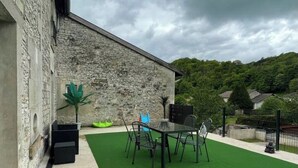 An outdoor patio with a table and chairs, a stone building, and a green artificial turf area. - Small house in the country, with terrace!  Pets allowed. (Osne-le-Val)