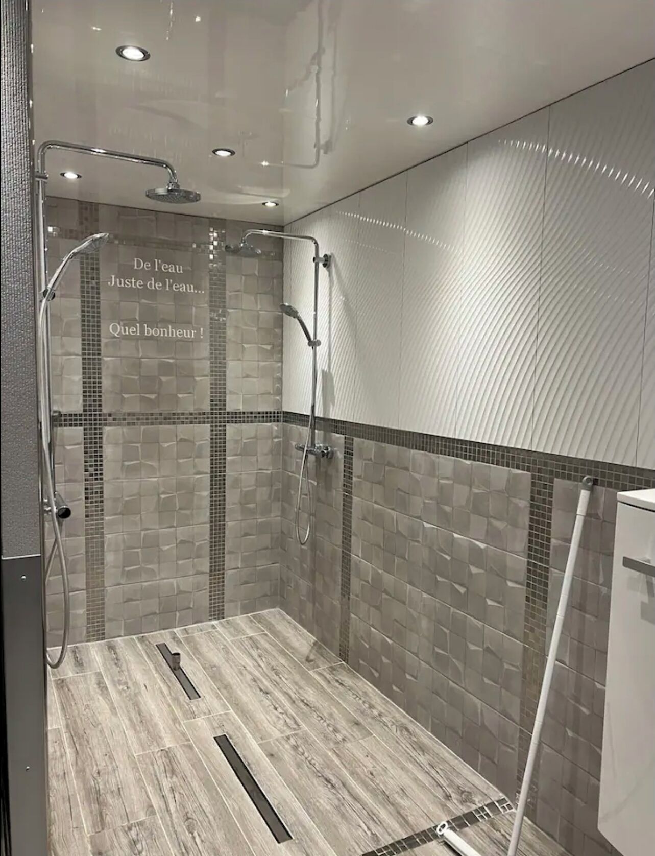 A modern shower with a glass door, tiled walls, and a wooden floor.