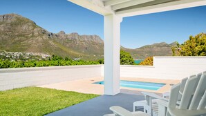 Un espacio exterior techado con piscina, sillas blancas y vistas a montañas y un pueblo.
