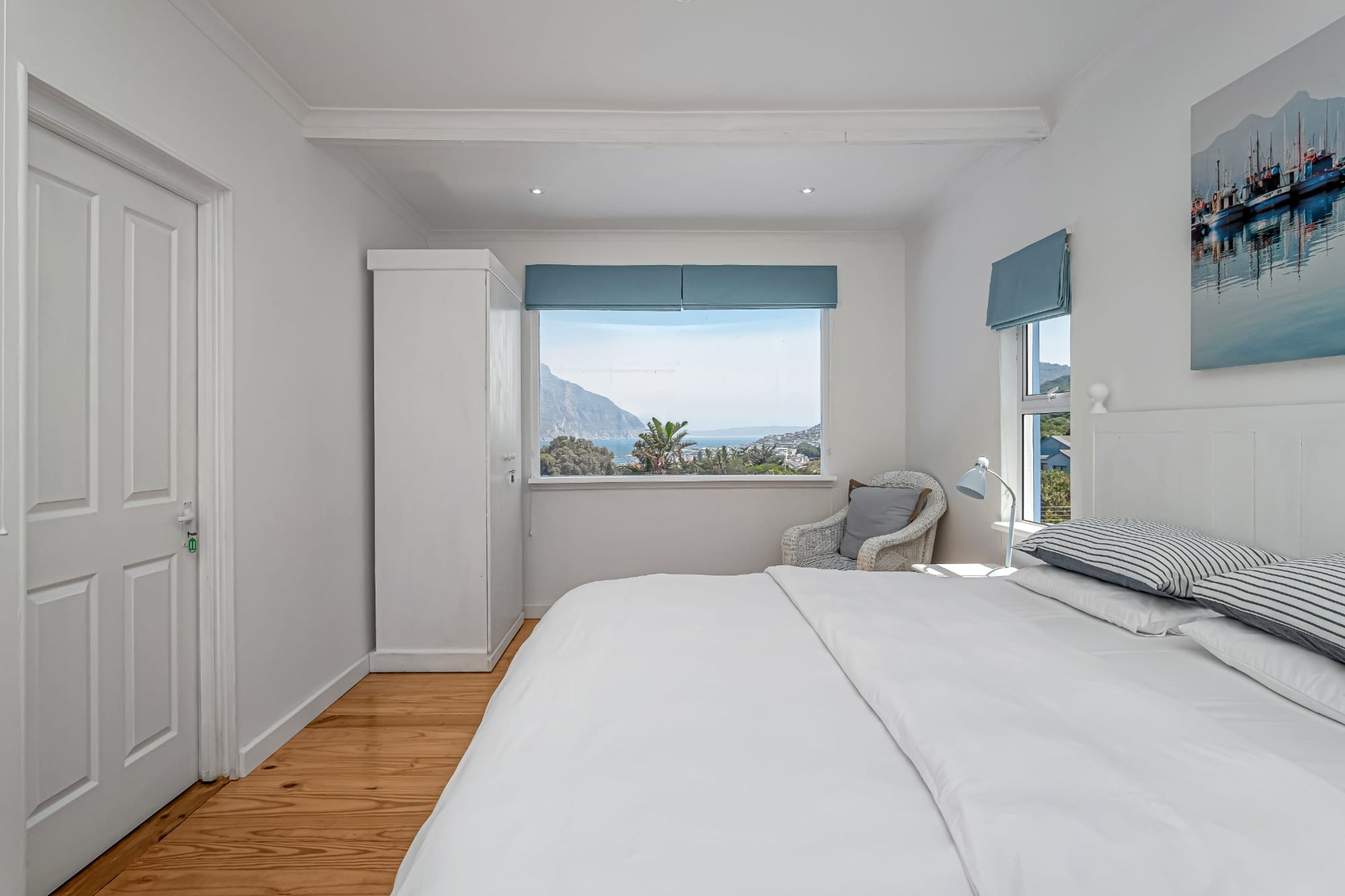 A bedroom with a large bed, a view of the sea, a chair, and a door.