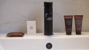 A bathroom sink with a shower head, two bottles of Botanica hair care products, and a Botanica shower cap. - Il Vicoletto B&B in centro (Ciro Marina)