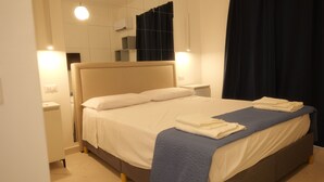 A neatly made bed with a headboard, bedside tables, and a wall-mounted air conditioner. - Il Vicoletto B&B in centro (Ciro Marina)