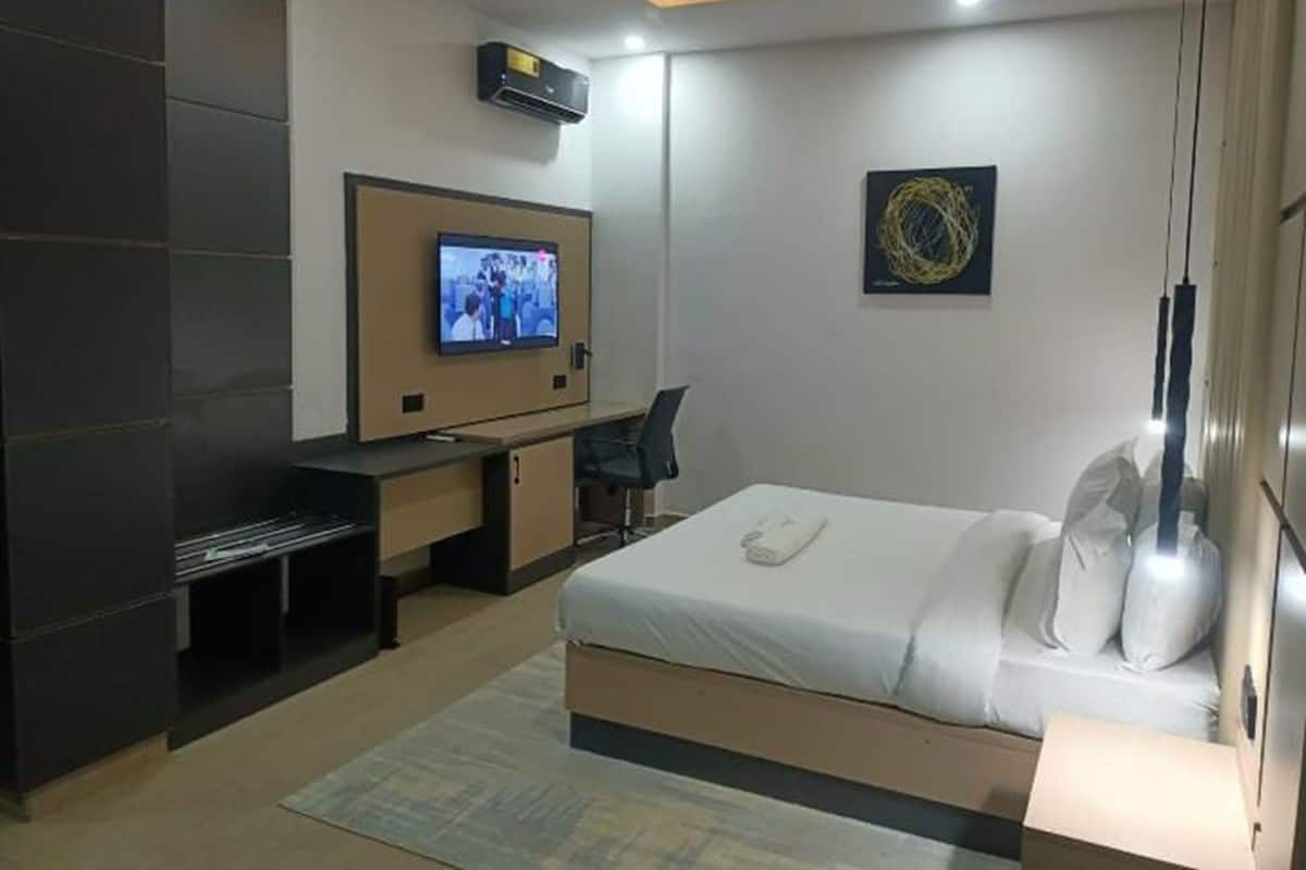 Une chambre d’hôtel moderne équipée d’un lit, d’un bureau, d’une télévision et d’un climatiseur fixé au mur.