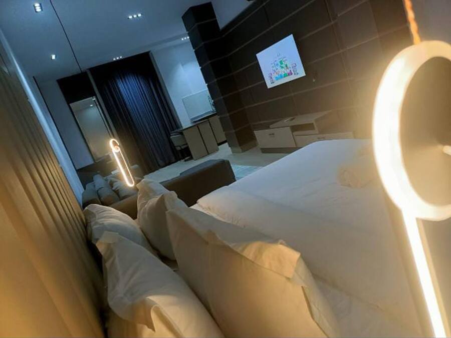 A modern hotel room with a large bed, a TV mounted on the wall, and a bedside table.