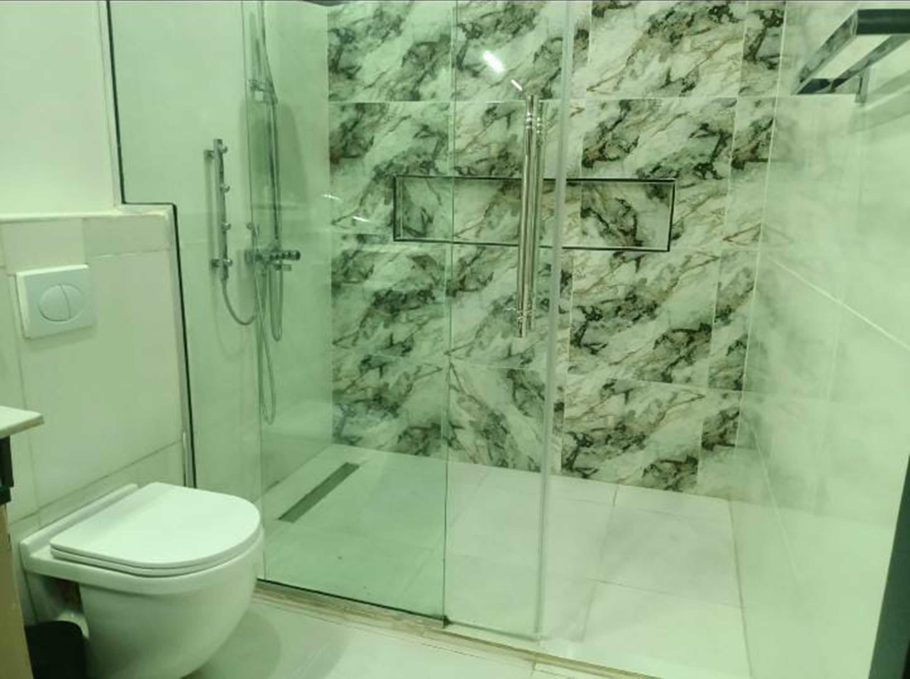 Une salle de bain avec une douche à parois de verre, des toilettes et des murs décorés d’un motif imitant le marbre.