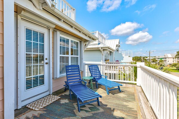 A covered porch with two blue lounge chairs, a small table, and a white railing.
