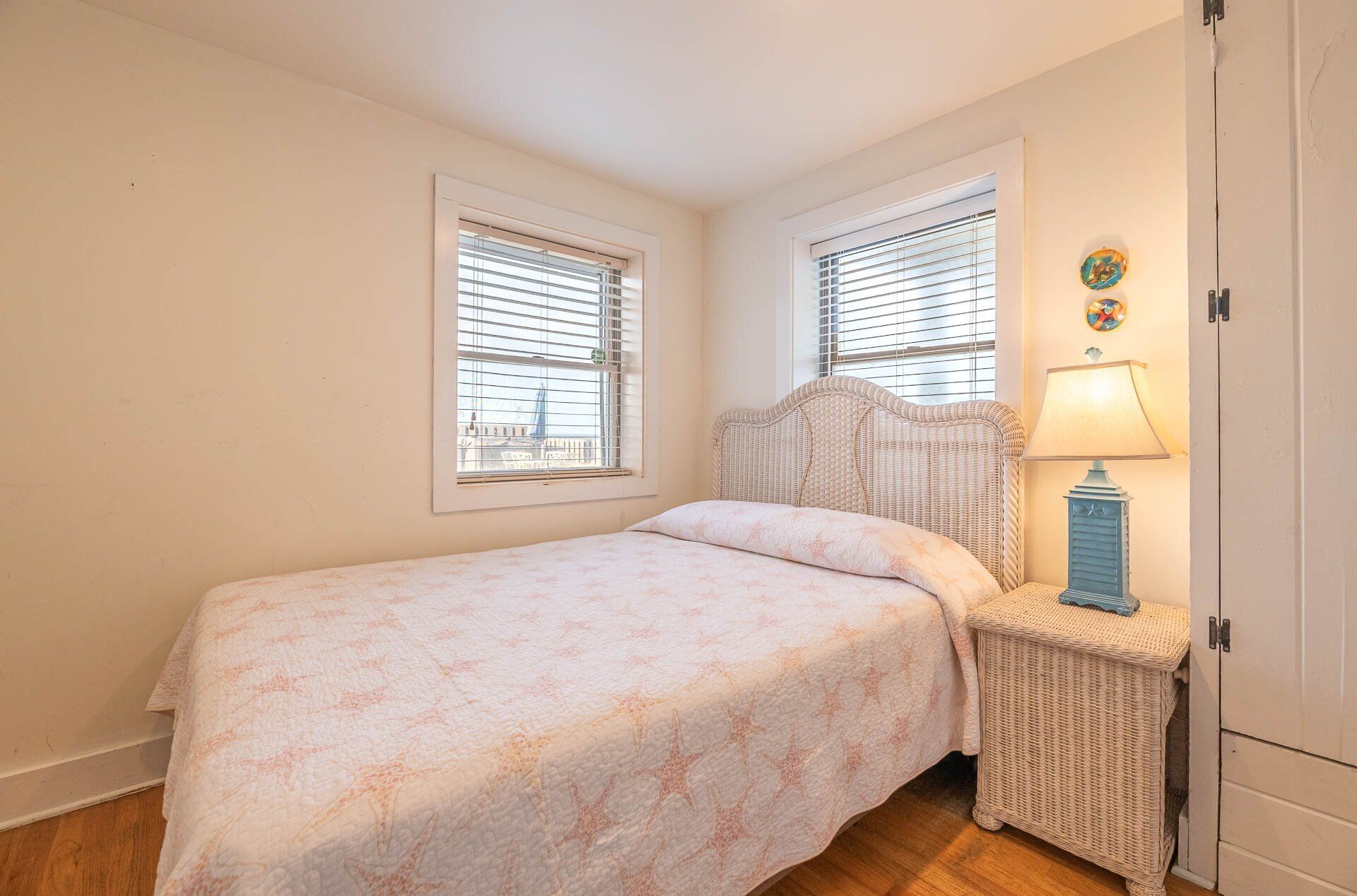 A bedroom with a bed, two windows, a nightstand with a lamp, and a wardrobe.