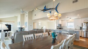 A spacious living area with a large wooden dining table, white chairs, a grey sofa, and a ceiling fan. - Dune Crest - Southern Shores, Oceanfront, Pool, Hot Tub, Pool Table, Pets OK (Southern Shores)