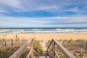 A wooden boardwalk leading to a sandy beach with ocean waves in the background.