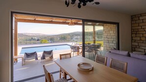 A modern dining area with a view of a swimming pool and hills.