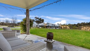 An outdoor patio with wicker furniture, a decorative urn, and a view of a modern house in the background. - Limestone Views: Discover this farmhouse set in a bend of the Tambo River (Swan Reach)