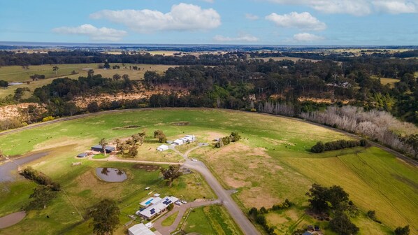 Vista aérea de una propiedad rural con un gran campo abierto, un pequeño estanque y varias construcciones, incluyendo una casa y un granero.