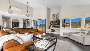 A spacious living room with leather sofas, a coffee table, and large windows offering a view of the outdoors. - Limestone Views: Discover this farmhouse set in a bend of the Tambo River (Swan Reach)