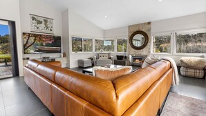 A modern living room with a large leather sectional sofa, a fireplace, and large windows offering a view of the outdoors. - Limestone Views: Discover this farmhouse set in a bend of the Tambo River (Swan Reach)