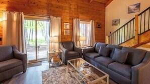 Un salon chaleureux avec un plafond en bois, un ensemble de canapés, une table basse et un escalier.