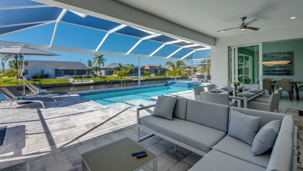 A modern outdoor living area with a pool, a sofa, and a dining table. - Villa Summer Feeling - newly built, on water, pool & spa (Cape Coral)