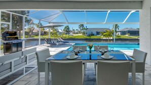 An outdoor patio with a table set for dining, overlooking a swimming pool and a residential area. - Villa Summer Feeling - newly built, on water, pool & spa (Cape Coral)
