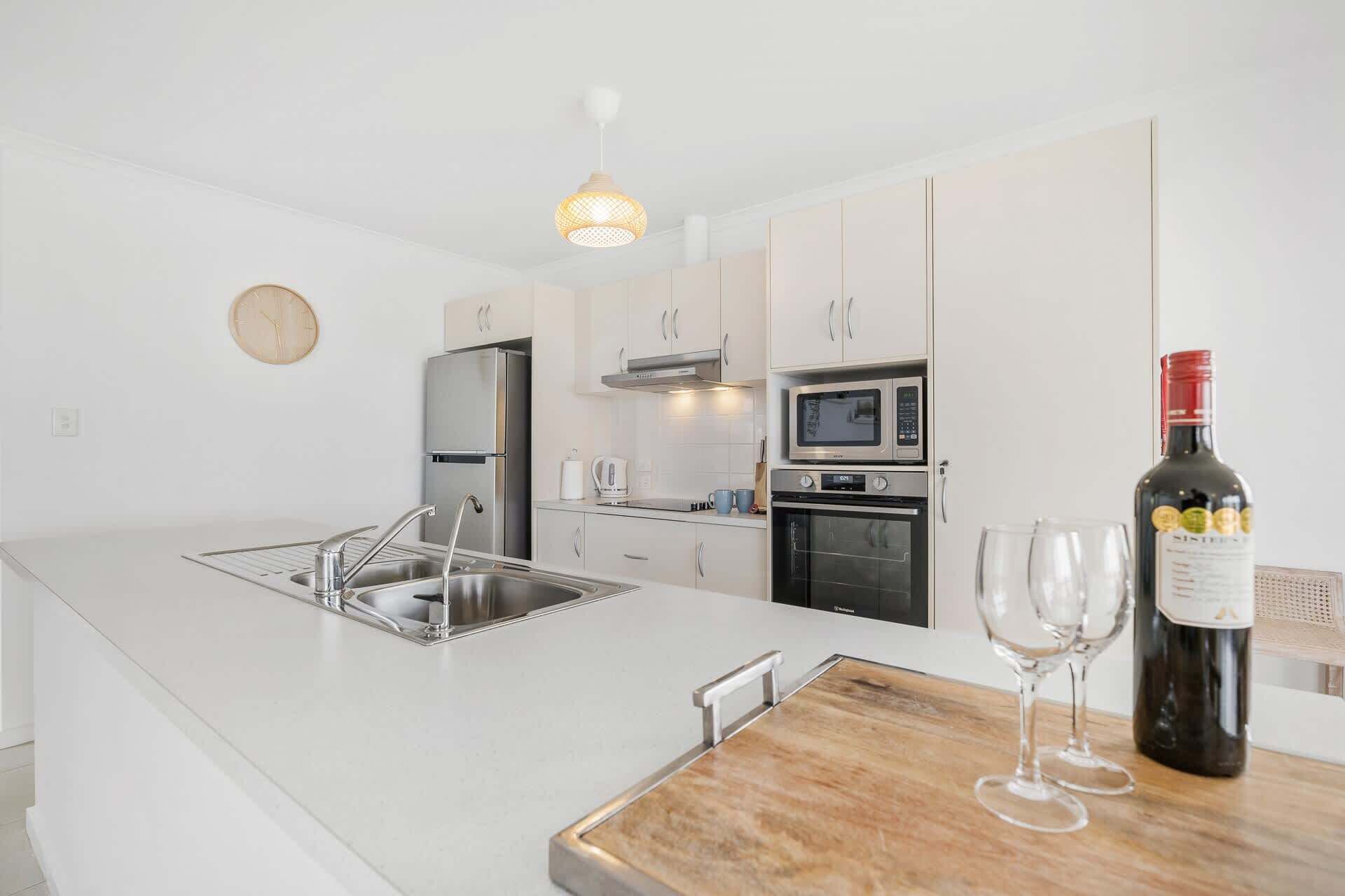 A modern kitchen with a central island, stainless steel appliances, and a wine bottle and glasses on the counter.