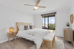 Une chambre à coucher comprenant un lit, une table de chevet, une lampe, un banc et une vue sur l’extérieur.