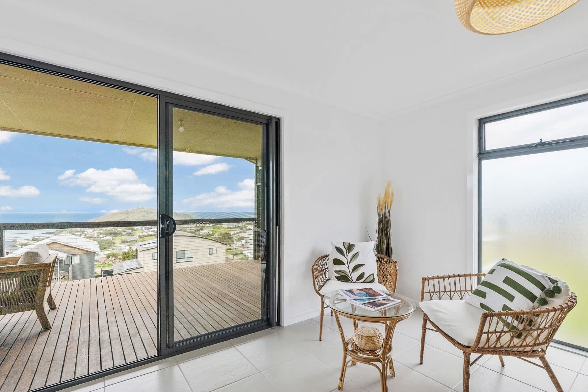 A balcony with a wooden deck, wicker furniture, and a glass door leading to a view of a residential area.