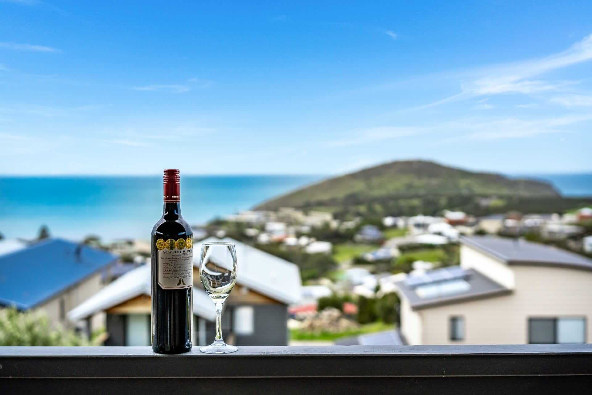 A bottle of wine and a glass on a balcony overlooking a coastal town.