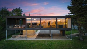Een modern huis met een glazen gevel, buitenmeubilair en een trap naar een hoger gelegen niveau.