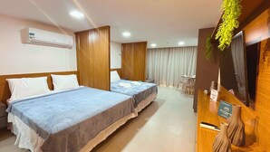 A hotel room with two beds, a desk with a TV, and a reception area. - Flat FM20 Vista Lateral - By Almare (João Pessoa)