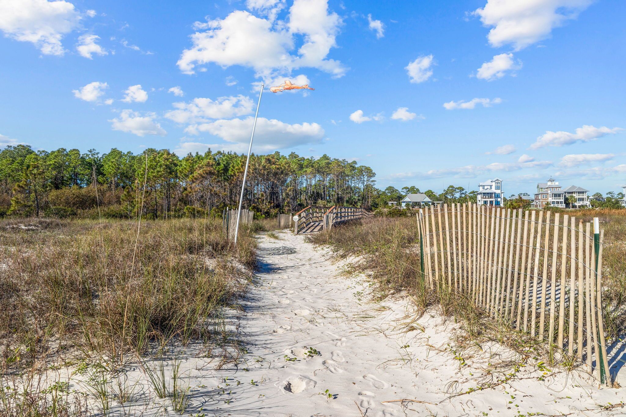 A sandy beach path leading to a wooden fence with a beach house in the background.