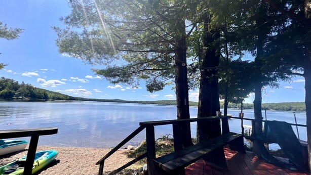 A lakeside deck with kayaks, a wooden bench, and a view of the lake and distant hills.